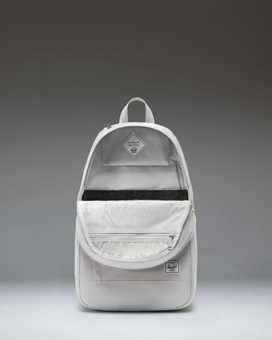 A light grey Herschel Seymour Backpack in the color Metal, featuring dual side pockets and the signature brand logo on the bottom left.