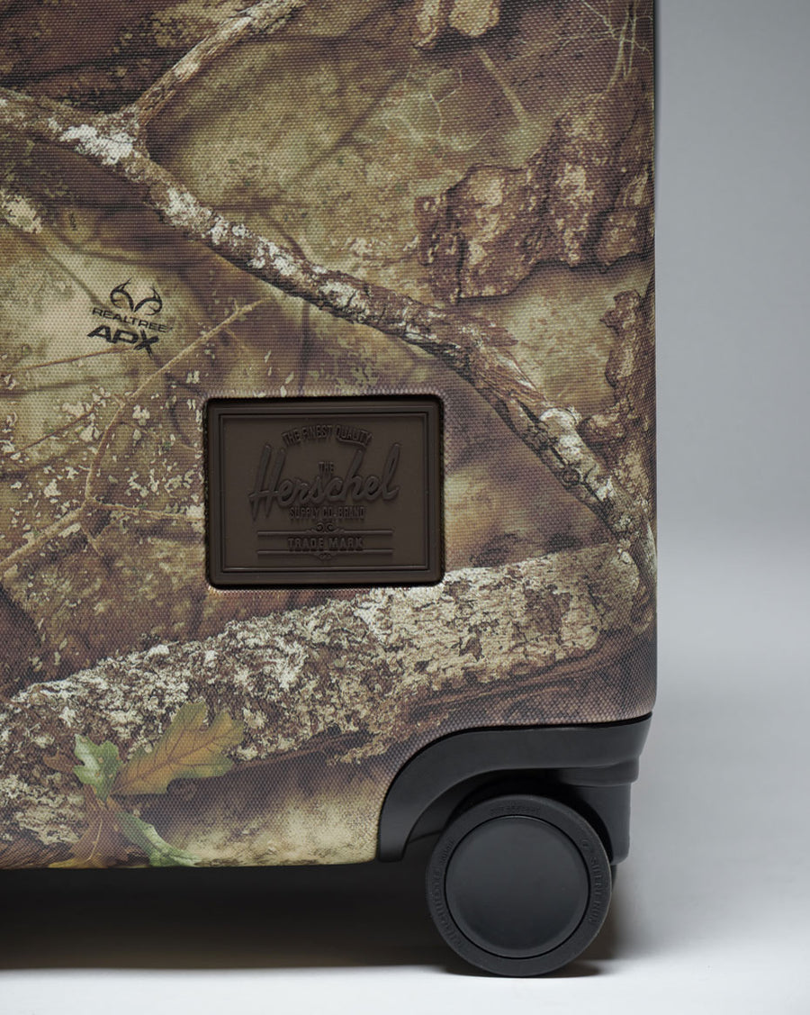 Herschel Heritage Carry On Luggage in Realtree APX Camo pattern, featuring a distinctive camouflage print.