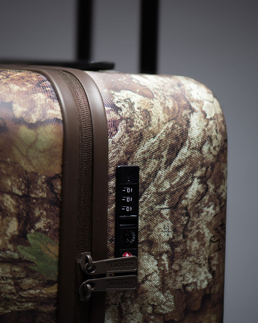 Realtree Herschel Heritage Large CO Luggage featuring a Realtree APX Camo pattern design.