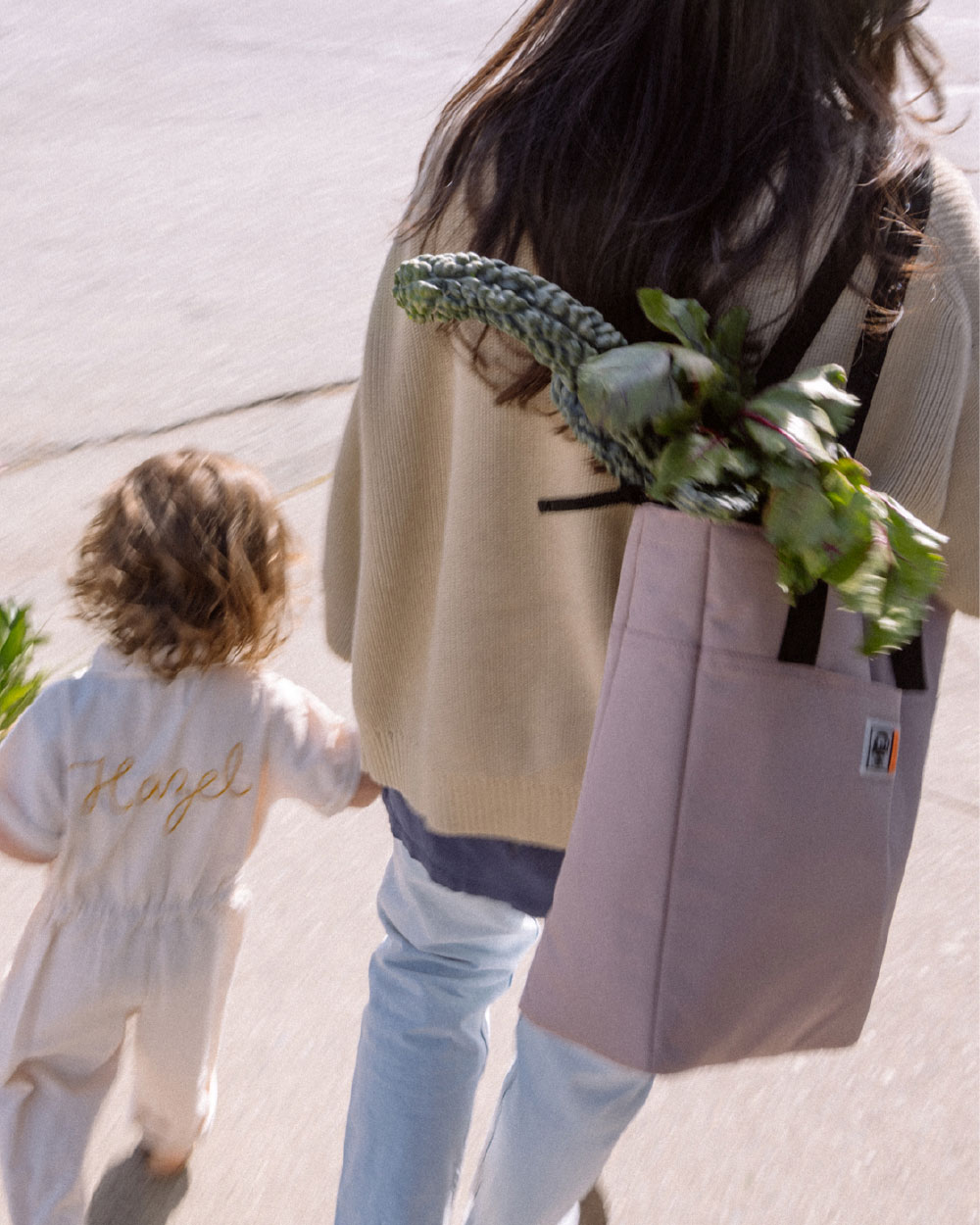 woman with a insulated tote full of groceries walks with her infant daughter.