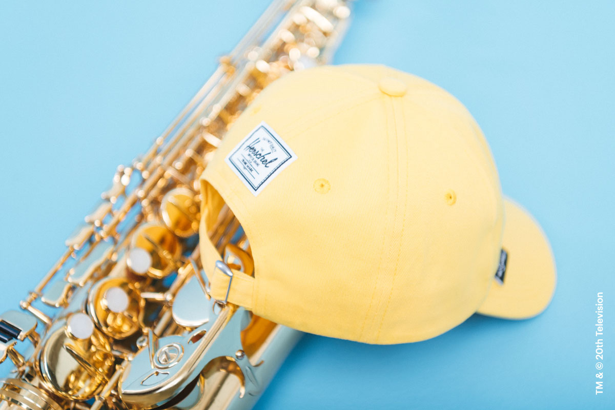 The back of the Sylas Cap Simpsons in Lisa Simpson print on top of a saxophone showing the Herschel Supply Company woven label