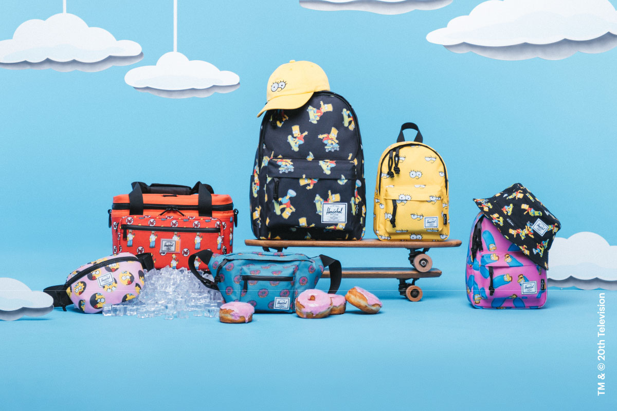 A group shot of a bunch of The Simpsons™ x Herschel Supply Company products against a blue background with white clouds hanging from the sky.